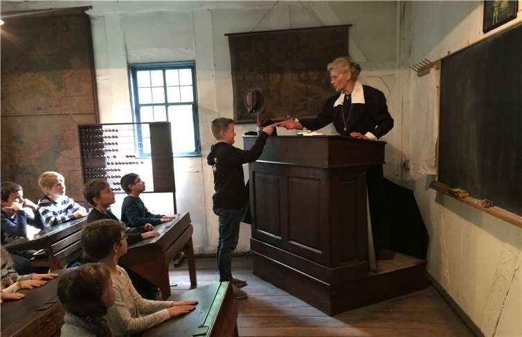 Ein Junge geht zum Katheder der Lehrerin und erhält ein Fleißkärtchen.