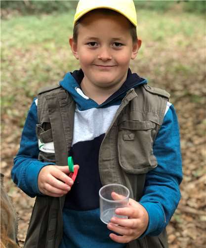 Ein Schüler zeigt stolz seine schwangere Wolfsspinne in der Becherlupe.