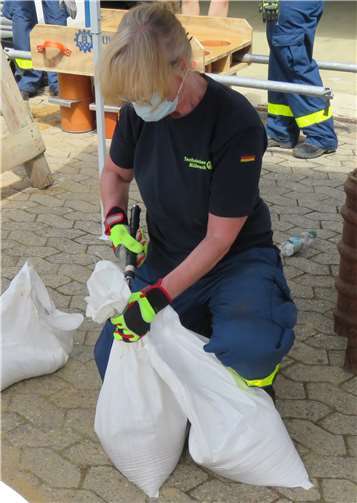 Eine THW-Helferin verschließt die Öffnung des Sandsackes, damit dieser beim Verlegen keinen Sand verliert..