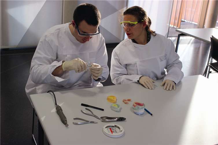 Eine Zahntechnikerin bringt ihrem Lehrling das Herstellen eines Befestigungselementes für eine Teilprothese bei.