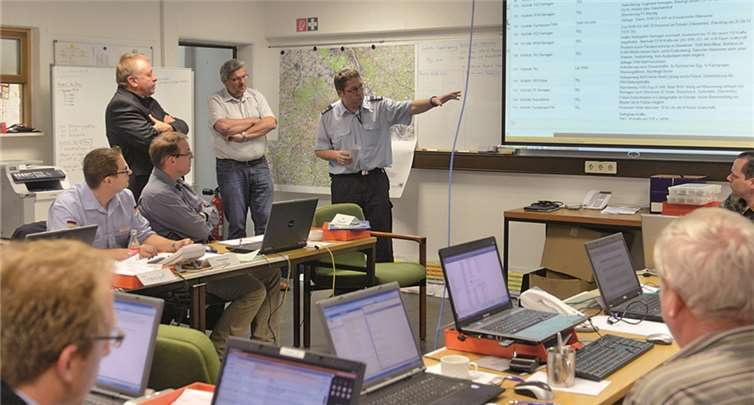 Einsatztagebuch an der Wand, Laptops auf den Tischen: Michael Zimmermann (stehend rechts) erläutert die Abläufe der TEL-Übung, Dr. Jürgen Pföhler (stehend links) weiß den Katastrophenschutz in guten Händen. Kreisverwaltung Ahrweiler