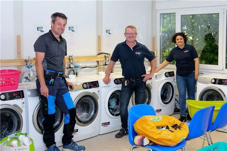 Elektromeister Tim Weber (li.) hat mit der kostenlosen fachgerechten Erweiterung der Elektroinstallation im Waschsalon vom DRK-Fluthilfe Beratungs- und Servicecenter Ahr geholfen, die Waschkapazitäten dem gestiegenen Bedarf anzupassen und von vier auf acht Waschmaschinen zu verdoppeln. Michael Kluge-Dummer (Mitte) und Sana Daghfous vom DRK-Kreisverband Ahrweiler e.V. freuen sich über die tatkräftige Unterstützung zum Wohle der flutbetroffenen Mitbürger.  Foto: Thorsten Trütgen