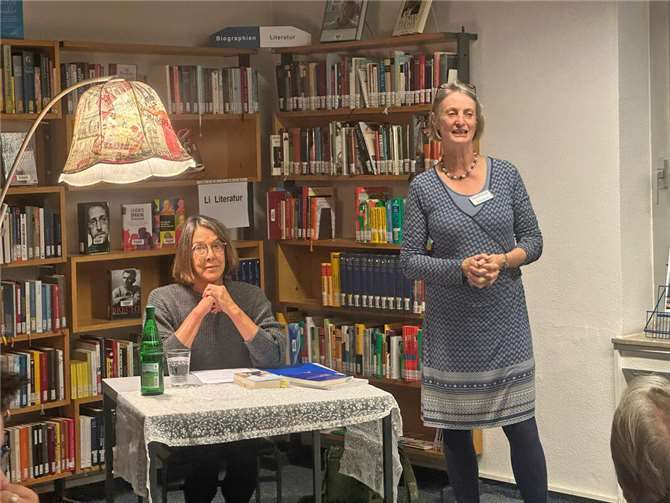 Franzis Steinhauer, Leiterin der Bücherbrücke Meckenheim/Alfter, begrüßt das Publikum zur Lesung von Autorin Sabine Trinkaus (sitzend). Foto: Stadt Meckenheim