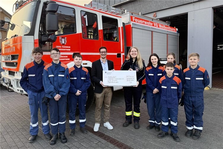 Freudige Gesichter bei der symbolischen Scheckübergabe zur 500 Euro-Spende mit Thorsten Escher, Geschäftsstellenleiter der Sparkasse Koblenz in Weißenthurm, der Jugendfeuerwehrwartin Sarah Gerolstein und denJungen und Mädchen der „Thurer“ Jugendfeuerwehr.