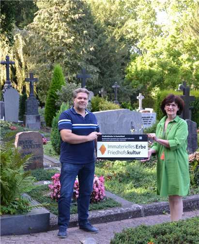 Friedhofskultur ist Immaterielles Kulturerbe: Andreas Drechsler, Werkleiter des Eigenbetriebs Grünflächen- und Bestattungswesen und Rita Reusch, Leiterin des Bestattungswesens, präsentieren ein neues Schild auf dem Hauptfriedhof. Foto: privat