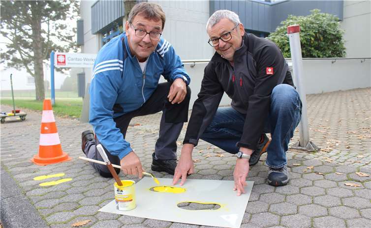 Für mehr Sicherheit: Mit Hilfe einer Schablone brachten Helmut Reimann (rechts), Fachkraft für Arbeitssicherheit beim Caritasverband Westerwald-Rhein-Lahn, und Hausmeister Andreas Wirthwein gemeinsam die gelben Füße auf dem Bürgersteig vor den Caritas-Werkstätten in der Montabaurer Warthestraße auf.  Caritas