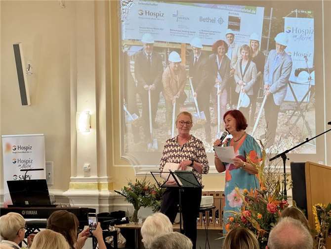 Gabriele Ruggera (links), Hospizleiterin und Geschäftsführerin der Hospiz im Ahrtal gGmbH, und Ulrike Dobrowolny (rechts), Vorsitzende des Hospiz-Vereins Rhein-Ahr, begrüßen die Gäste im festlichen Rathaussaal (Projektion im Hintergrund zeigt den Spatenstich zum stationären Hospiz). Foto: Hospiz im Ahrtal gGmbH (Andrea Simons)