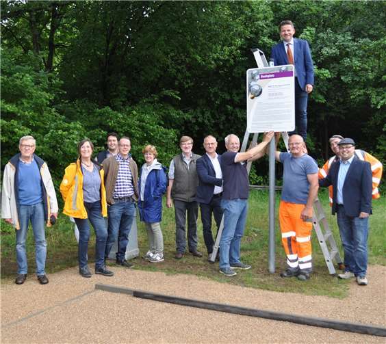 Gemeinsam mit dem Vorsitzenden des UWG-Stadtverbandes Hans-Erich Jonen (unten 4.v.r.) und den Mitarbeitern des Baubetriebshofes (in oranger Kleidung) um ihren Leiter Ullrich Hagedorn (unten 5.v.r.) bringt der Erste Beigeordnete Holger Jung das Schild für die neue Boule-Anlage an. Foto: Stadt Meckenheim