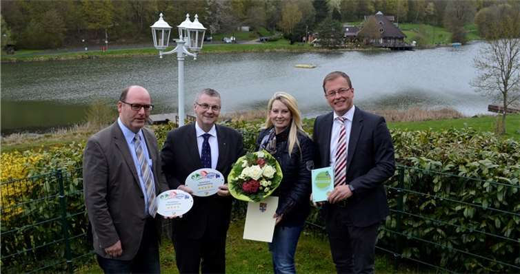 Gratulierten Beate Dahm-Schmitz zur neuerlichen Klassifizierung mit 4 und 5 Sternen und der Auszeichnung „Qualitätsgastgeber“ für das Ferienhaus Chalet am Waldsee in Rieden. Vor dem herrlichen Panorama des Riedener Waldsee, im Garten des Hauses: Riedens Ortsbürgermeister Andreas Doll, Landrat Dr. Alexander Saftig, und Verbandsbürgermeister Jörg Lempertz, gleichzeitig auch als Verbandsvorsitzender des Zweckverband Ferienregion Laacher See. Privat