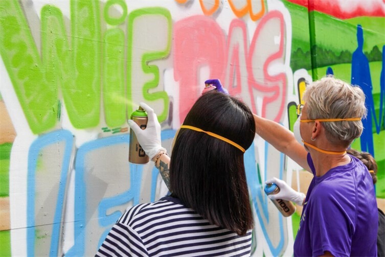 Hauptamtliche und ehrenamtliche Mitarbeiter greifen selbst zur  Spraydose unter Anleitung von Graffiti-Künstler Daniel Schmitz. So bunt wie das Leben – und so bunt wird auch unsere Wand!