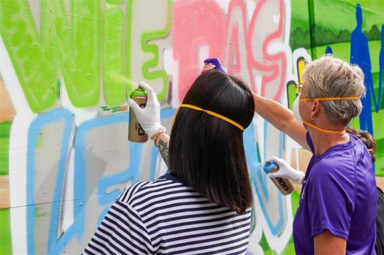Hauptamtliche und ehrenamtliche Mitarbeiter greifen selbst zur Spraydose unter Anleitung von Graffiti-Künstler Daniel Schmitz. So bunt wie das Leben – und so bunt wird auch unsere Wand!
