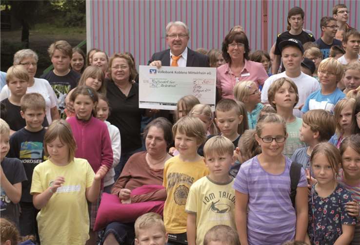 Heinz Engels (Mitte) und Claudia Kietzmann (re. daneben), Lill Brückmann (li. daneben) und freiwillige Helfer inmitten der Kinder der Sommerferienfreizeit Harterscheid.Volksbank Koblenz Mittelrhein
