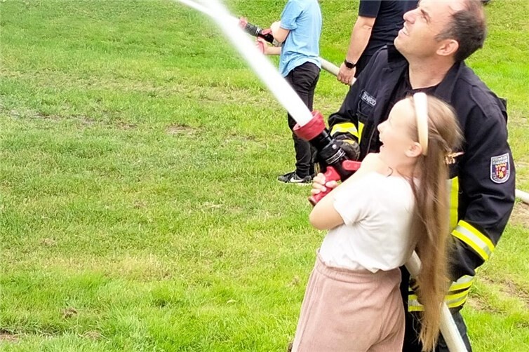 Herr Tobias Schaarschmidt mit einer Drittklässlerin beim Spritzen  mit dem Feuerwehrschlauch