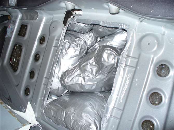 Hier ist der Blick aus dem Fahrzeuginneren auf die Öffnung in der Rücksitzbank zu sehen. Man sieht, wie die Schnittkanten mit Klebeband abgeklebt sind. In der Öffnung sieht man einige der Pakete, die mit Marihuana gefüllt waren.