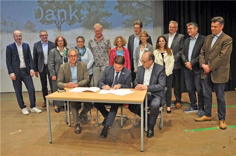 Im Beisein von Vertreterinnen und Vertretern der Schulen, Stadtverwaltung und Projektpartner unterzeichnen Bürgermeister Holger Jung (vorne Mitte), Bert Sluyter von Ten Brinke Bau GmbH & Co. KG (links) und der Technische Beigeordnete Heinz-Peter Witt (rechts) den Vertrag für das Millionenprojekt am Schulcampus. Foto: Stadt Meckenheim