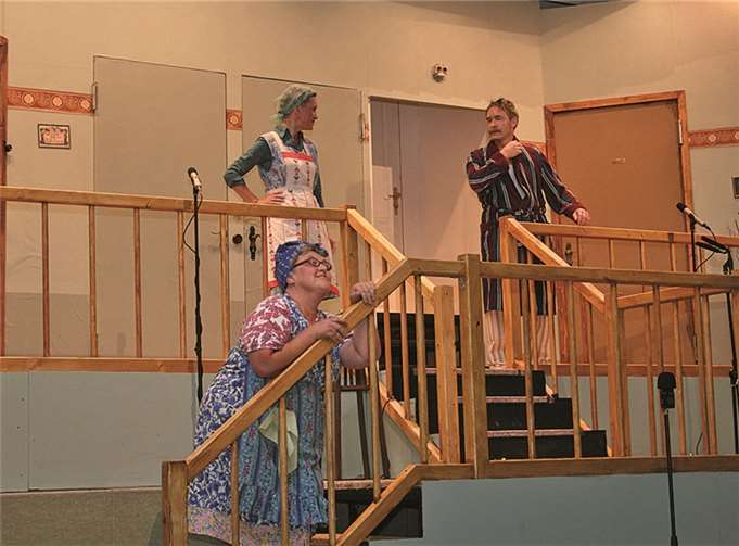 Im Bild vorne liegt Klatschtante Meta Bold (Melanie Decker) im Treppenhaus auf der Lauer, um die Wohnungsnachbarn Hanne Knoop (Rita Friedrich) und Ewald Brummer (Klaus Erler) zu belauschen.