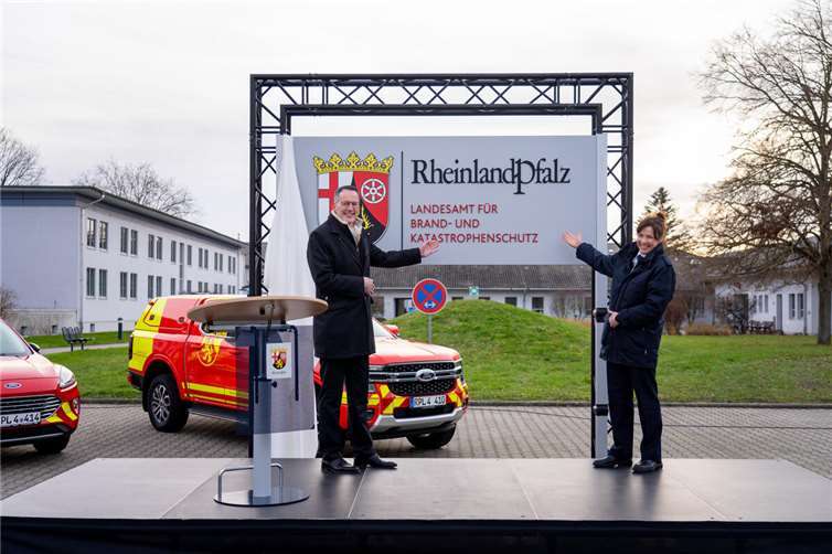 Landesamt für Brand- und Katastrophenschutz nimmt Arbeit auf Innenminister Michael Ebling und Landesbrand- und Katastrophenschutzinspekteurin Kirstin Eisenhauer mit dem Schild der neuen Behörde. Im Hintergrund stehen landeseigene Einsatzfahrzeuge im neu gestalteten Design. Foto: Innenministerium RLP