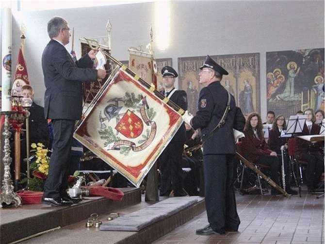 Innenminister Roger Lewentz überreicht Fahnenträger Wilfried Kalmund das Banner für langjährige Teilnahme an der Feuerwehrwallfahrt. privat
