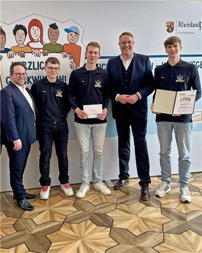 Jannik Soetebier (2.v.l.), Fin Wissen (Mitte) und Mika Wissen (rechts) vom Junggesellenverein Bell nahmen den Preis von Ministerpräsident Alexander Schweitzer (2.v.r.) und im Beisein des Ersten Kreisbeigeordneten Pascal Badziong (links) entgegen.  Foto: Staatskanzlei RLP/Schäfer