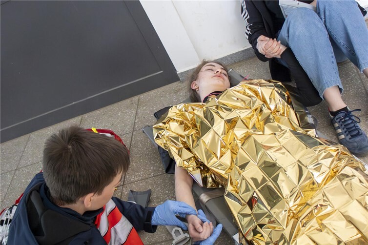 Jugendliche Einsatzkräfte der Malteser Jugend versorgen im Rahmen der Übung eine verletzte Person und schützen sie mit einer Rettungsdecke vor Unterkühlung.
