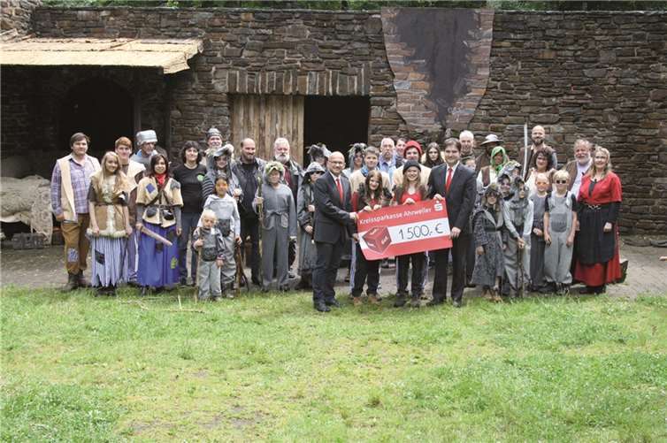 KSK-Marktbereichsleiter Christoph Frings (vorne links) und KSK-Geschäftsstellenleiter Wolfgang Kaspers (vorne rechts) überreichen Ronja Räubertochter und den weiteren Aktiven der Freilichtbühne Schuld den symbolischen Scheck über 1.500 Euro. KSK