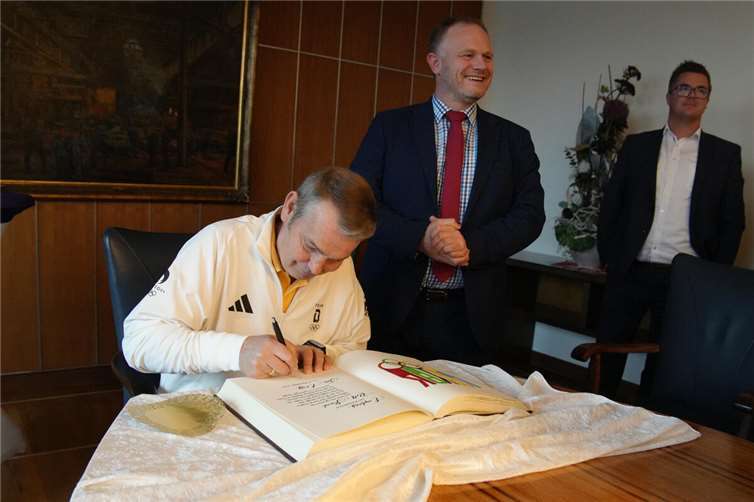 Kanu-Bundestrainer Ralf Straub trägt sich vor den Augen von Neuwieds Oberbürgermeister Jan Einig und Bürgermeister Peter Jung (v.l.n.r.) ins Goldene Buch der Stadt ein.  Foto: Felix Banaski