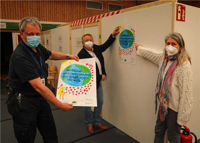 Klaudia Hendricks (re.), Präsidentin des gemischten Rotary Clubs Koblenz Mittelrhein, brachte gemeinsam mit Bürgermeisterin Ulrike Mohrs und Impfkoordinator Olav Kullak die ersten Plakate der Grundschule Wallersheim im Impfzentrum Koblenz an.Foto: Stadt Koblenz/Egenolf