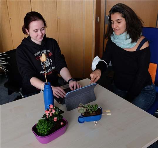 Lisa Höfer (li.) und Dr. Zuhal Gültekin blicken auf eine Deko-Schubkarre, die aus einer Butterdose, aus Flaschendeckeln und Schaschlikspießen gefertigt wurde; der Blumentopf war einst eine Eisschachtel, die Vase eine pfandfreie Flasche.Foto: Stadt Neuwied