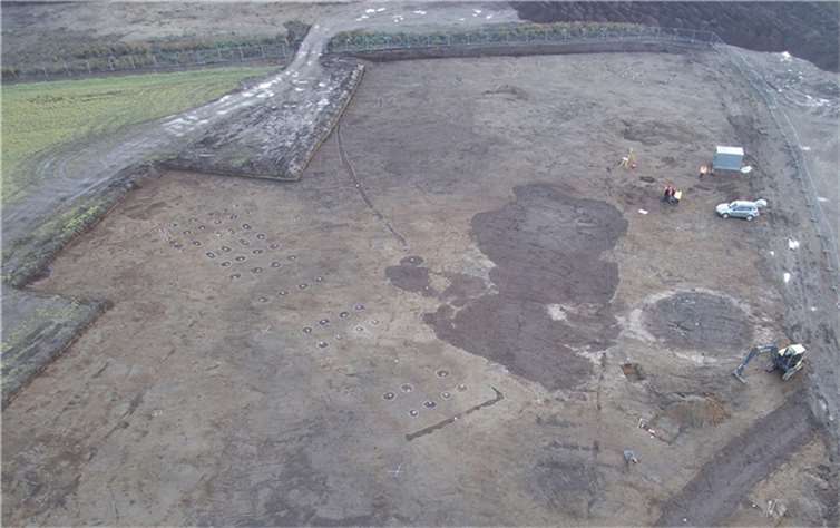 Luftbild von Norden über einen Teil der Grabungsfläche. Vorne links der Pfostengrundriss eines bandkeramischen Langhauses mit Resten eines Wandgrabens vor der nordwestlichen Giebelseite. Gesamtlänge ca. 43 m. Die große unregelmäßige Bodenverfärbung in der Bildmitte ist eine neuzeitliche Lehmentnahmegrube, die kreisförmige Verfärbung rechts daneben ein verfüllter Bombentrichter aus dem 2. Weltkrieg. Foto: GDKE, Direktion Landesarchäologie, Außenstelle Koblenz / M. Gensty