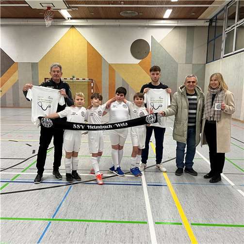 Martin Möllmeier, Cheftrainer U11-Junioren (v.l.), und motivierte Kicker der U11 bedanken sich bei Initiator und Spielervater Osama Hadad, Arzt im Herz-Jesu-Krankenhaus, und der Kaufmännischen Direktorin des Krankenhauses, Carmen Elschner, für die neuen Trikotsets.  Foto: Martin Reuschenbach/©Dernbacher Gruppe Katharina Kasper