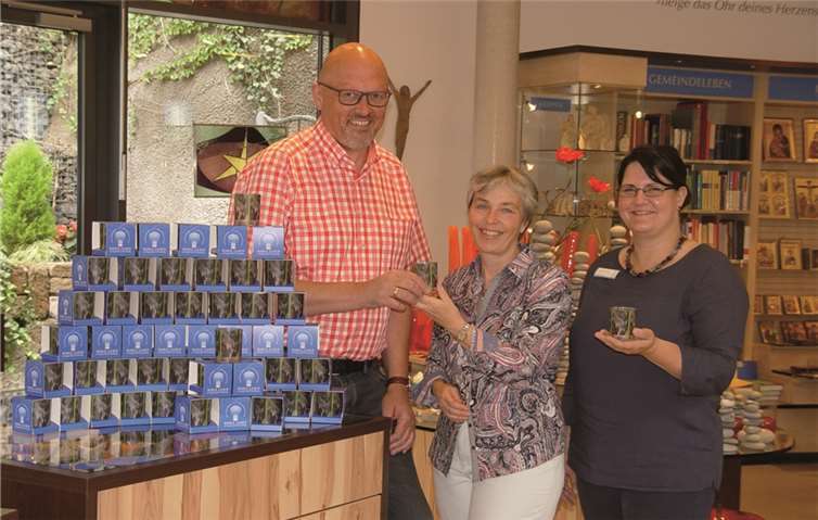 Matthias Wilken, Leiter der Buch- und Kunsthandlung, und Sandra Friedrich, Leiterin der Abteilung Kunst, überreichen Irmgard Hillesheim (M.) Schmucklichter aus Maria Laach.E.T.Müller