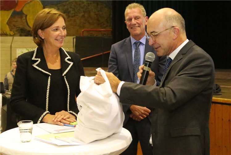 Mit einem Sack Äpfel bedankte sich BürgermeisterBert Spilles bei Bildungsministerin Yvonne Gebauer,Rektor Peter Hauck im Hintergrund.