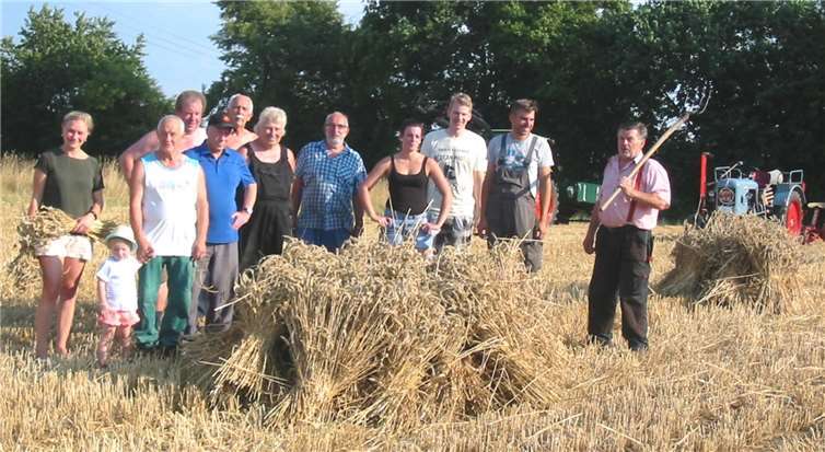 Nach getaner Feldarbeit posieren die fleißigen Arbeiterneben den aus Garben zusammengestellten Hausten.