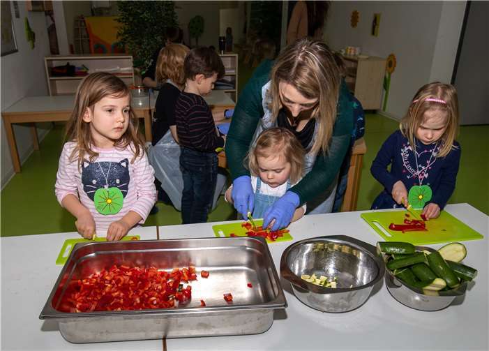 Nele (5), Marleen (3) und Charlotte (4) schneiden zusammen mit ihrer Erzieherin konzentriert Gemüse.