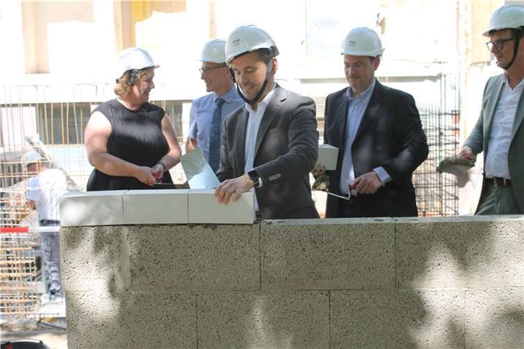 OB Langner bei der Verlegung seines Grundsteins, im Hintergrund machen sich Dezernent Ingo Schneider und Architekt Guido Fries sowie Schulleiter Schulte-Melchior und Julia Özdemir von der ADD bereit „ihre“ Grundsteine zu legen. Foto: Stadt Koblenz/T. Knaak