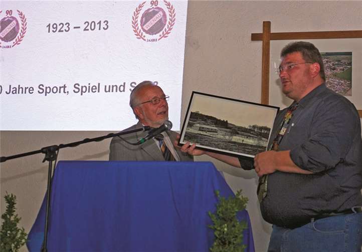 Ortsvorsteher Ernst-Günther Weßler übergibt Jens Kolbe ein Foto, auf dem noch die alte Sportanlage mit dem Schwimmbad zu sehen ist.