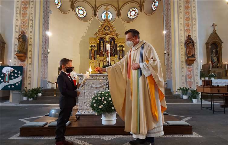 Pfarrer Norbert Missong entzündet mit dem Licht der Osterkerze, das noch vom Osterfeuer der Osternacht brennt, die Kommunionkerze von Damian Collet.