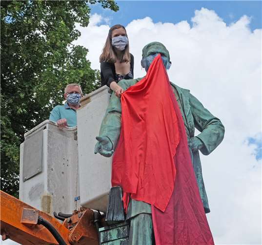 Pfarrerin Julia Arfmann-Knübel von der Evangelischen Friedenskirchengemeinde Neuwied hat die letzte „Schutz“-Maske an der Raiffeisen-Statue angebracht, die aus einem Mix von durchsichtigem Kunststoff und in zwei unterschiedlichen Rot-Tönen gehaltenem Tuch besteht.Foto: Stadtverwaltung