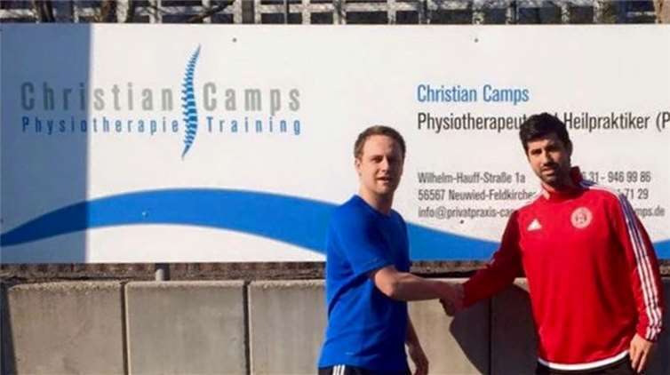 Physiotherapeut Christian Camps (l.) und Benedikt Stollhof präsentieren die am Sportplatz neu angebrachte Werbebande.privat