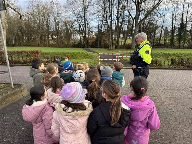„Praxisübung auf der Straße“: Die Kinder üben unter Anleitung von Polizeihauptkommissar Olaf Krüger das sichere Überqueren der Fahrbahn und wenden die erlernten Regeln direkt an.