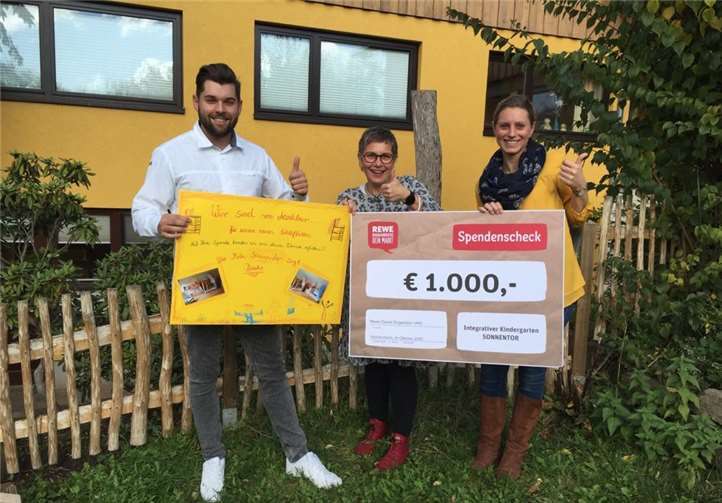 REWE-Marktleiter Tim Thermann (l.) nahm sich extra Zeit, um dem Kindergarten zur Übergabe des symbolischen Spendenschecks einen Besuch abzustatten. Die Kinder bedankten sich mit einem selbst gestalteten Plakat, welches durch Sonja Muth (Leitung des Kindergartens, Bildmitte) sowie Stefanie Schmitz (Vorstand des Kindergartens) überreicht wurde. Foto: Birgit Lind