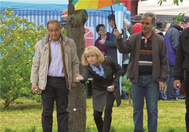 Regengeschützt unter buntem Schirm wirft die Bürgermeisterin die erste Boule-Kugel. Norbert Girmann / Thomas Rittgen