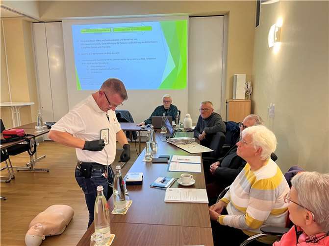Rettungsassistent Michael Kluge-Dummer (li.) demonstrierte dem Seniorenbeirat die Handhabung und die Funktionsweise von automatisierten externen Defibrillatoren (AEDs) und erklärte, dass grüne Schilder mit einem weißen Herzsymbol in der Mitte auf freizugängliche Laien-Defibrillatoren hinweisen. Foto: Astrid Zens / DRK-Kreisverband Ahrweiler e.V.