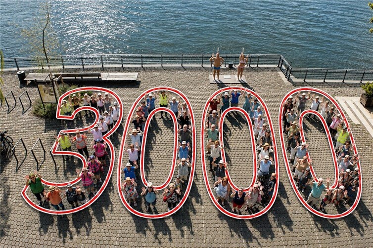 Rund 70 Teilnehmerinnen und Teilnehmer formierten sich an der Neuwieder Rheinpromenade zur Zahl „3000“ – dem Symbol der Lions-Aktion „3000 Schritte für Bewegung und Begegnung“. Das veröffentlichte Bild wurde mithilfe von Künstlicher Intelligenz (KI) grafisch überarbeitet, um die dargestellte Formation „3000“ besser sichtbar zu machen.