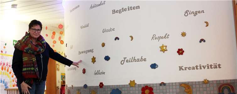 Sandra Schenkelberg, Interkulturelle Fachkraft in der Caritas-Kita St. Franziskus, vor dem neuen Wandbild im Flur der Wirgeser Einrichtung. Ein wichtiger Bestandteil des Kunstwerkes sind unter anderem die Gruppensymbole aus Keramik, die sie unter anderem gemeinsam mit den Kindern angefertigt hat. Foto: privat