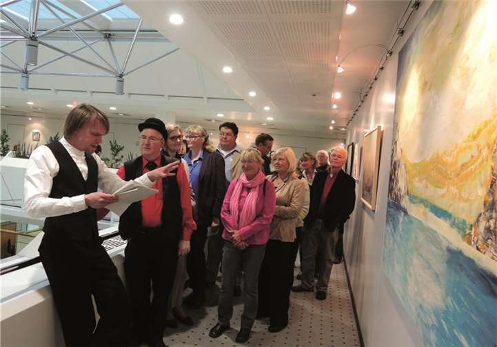 Schauspieler Jona Mues mit Moderator und Zauberer Andino sowie Gästen vor einem Bild des Künstlers.