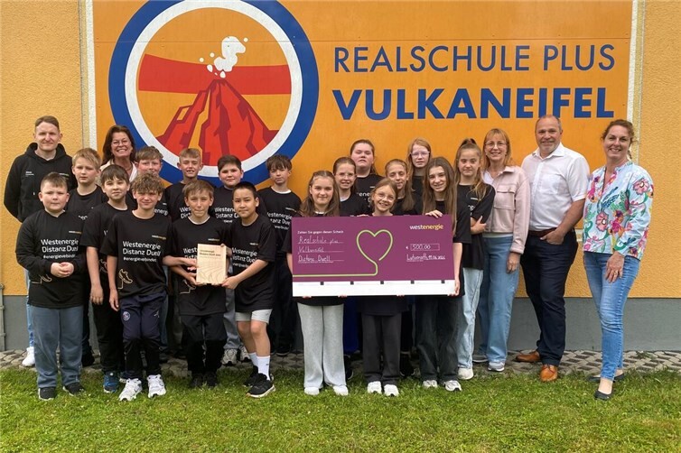 Scheckübergabe und Ehrung der schnellsten Klasse: Schülerinnen und Schüler der Klasse 5b der Realschule plus Vulkaneifel am Standort Lutzerath freuen sich gemeinsam mit Michaela Himberg, Sportlehrerin und Organisatorin (2. v. l.), Konrektorin Nadine Fresia (rechts) sowie Klassenlehrerin Iris Bauer (3. v. r.) über ihre Auszeichnung beim Westenergie Distanz Duell. Den Scheck überreichte Kommunalmanager Thomas Hau von Westenergie (2. v. r.). Alois Ebel, Mitarbeiter von Westenergie (links), unterstützte die Aktion als Profiläufer und Rekordhalter beim Distanz Duell.