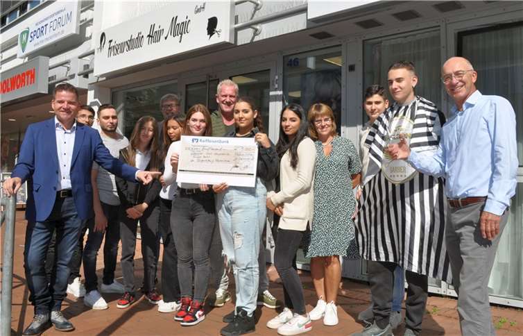 Scheckübergabe vor dem Friseurstudio Hair Magic: Bürgermeister Holger Jung (li.), Arkadii Wiens (3.v.li.), Thomas Radermacher (5.v.li.), Peter Hauck (8.v.li.) Marion Schrief-Viljoen (4.v.re.), Bert Spilles (re.) mit den Schülerinnen und Schülern des Wahlpflichtfaches.Quelle: Bürgerstiftung Meckenheim