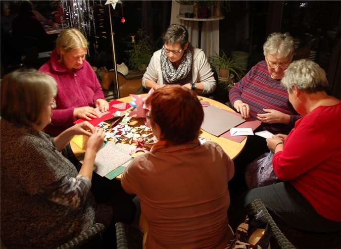 Sechs Mitarbeiterinnen beim Falten von Weihnachtssternen für den Verkauf auf hiesigen Weihnachtsmärkten.