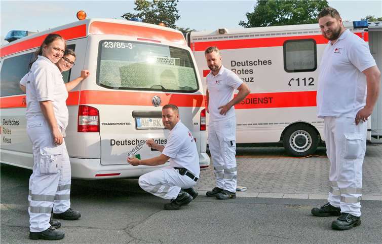 Stefan Bertram (knieend) bringt auf dem Heck eines Rettungsfahrzeugs des DRK-Rettungsdienstes im Ahrkreis den Kampagnenaufkleber an. Gemeinsam mit seinen diensthabenden Kolleginnen und Kollegen (v.li.) Tanja Schellhase, Jasmina Benamer-Belkacem, Tobias Kniel und David Weller demonstrieren sie stellvertretend für alle DRK-Rettungskräfte im Ahrkreis: Für unsere hilfebedürftigen Mitbürger sind wir #IMMERDA.Foto: privat